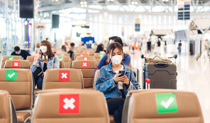 Young woman in quarantine for coronavirus wearing surgical mask face protection during virus pandemic with social distancing use smartphone typing message with luggage wait flight travel at airport