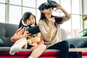 Portrait happy love asian family mother and little asian girl child smiling and using glasses of virtual reality headset metaverse.concept of modern technology