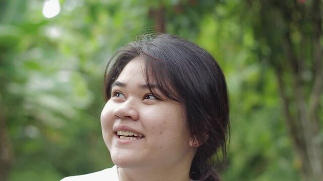 Portrait happy Asian plump face teen girl looking around in the natural park during summer. Close up cute chubby female teenager enjoy to stay in outdoor garden. Young lifestyle. Natural conservation.