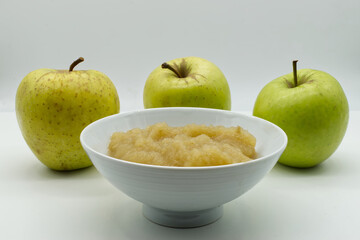 Apple sauce in a white bowl with raw apples on background. Apple puree and fresh green apples isolated on white background.