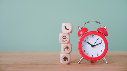 stack of contact us icon on wood cubes and red analog alarm clock on wooden desk and green...