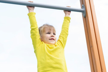 active little girl hanging on a horizontal bar in an open playground