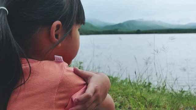 Cute upset little girl pouting on the lake road. Sad child sitting on road by the lake and waiting.