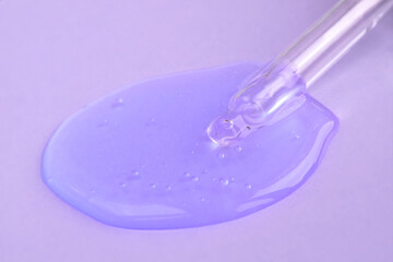 Pipette with fluid hyaluronic acid on violet background. Cosmetics, healthcare concept closeup. Dose of serum or retinol with air bubbles. Flat lay. Luxury gel or beauty product presentation in macro