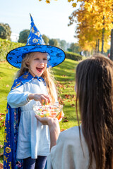 a woman treats a girl dressed as a witch with sweets. child takes sweets for the halloween holiday. trick or treat.