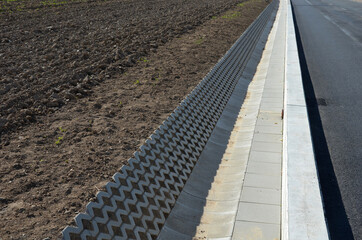 on the side of the road there is a concrete wall support and a ditch reinforced with perforated...