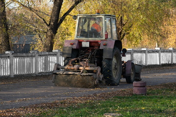 Sweeps the pedestrian sidewalk from dry leaves in autumn time. Vintage utility vehicle tractor with broom