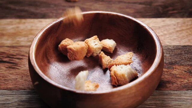 Crispy roasted bread croutons cubes falling in bowl in slow motion. Close up. Rustic view