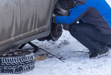 A man changes a wheel to a car in the snow