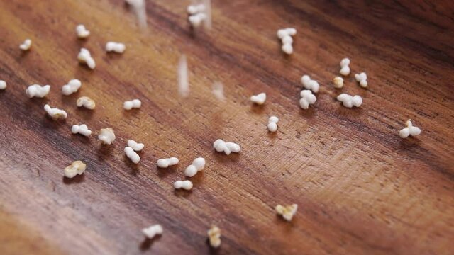 Amaranth popped, puffed dry grains falling on a rustic wooden surface in slow motion. Pseudocereal food, gluten free. Macro