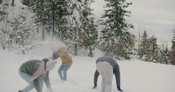 Group of friends playing snowballs and laughing enoying winter day in forest having fun together. Carefree youth and recreational activity concept.