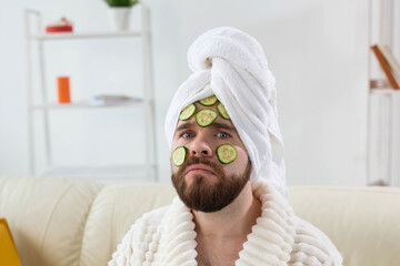 Bearded man holding cucumber slices on the face. Spa at home, body and skin care for male concept.