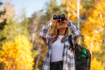 A female tourist walks through the autumn forest, looking through binoculars