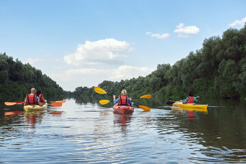 Fototapeta na wymiar Friends kayaking in summer river against trees and blue sky