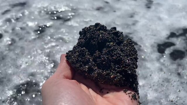 A handful of black sand in Vichada Black Sand Beach in Santorini, Greece