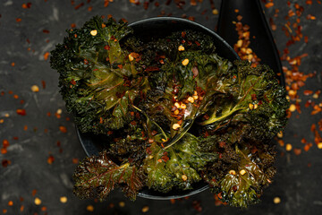 Kale salad baked chips with red chili pepper corns on dark background, vegan healthy snack, healthy food. Selective focus, copy space. 