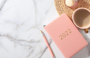 Pink coral colored diary for the year 2022, pen, coffee, macaron cookie on straw woven placemat