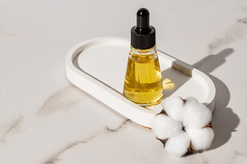 Natural organic beauty face oil in dropper bottle on concrete ctand with cotton flower on marble table. Unbranded presentation of skin care cosmetic products.