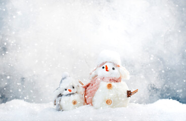 Christmas and new year snow concept with two cute snowmen in hats and scarves in snowdrift on gray background