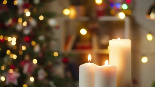 Burning candles close-up. Decorated christmas tree on background. Evergreen tree with garlands in living room. Winter holidays concept. Celebrating new year at home. 