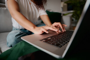 Fototapeta premium Close up of hands of a multi-ethnic female typing on laptop whilst sitting on the sofa