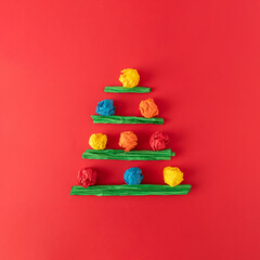 Christmas tree composition made of colorful paper on red background. Minimal flat lay holiday winter concept.