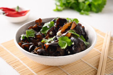 Salad of chinese pickled tree black muer mushrooms with chilli pepper and coriander leaves in bowl on white background. Close up.