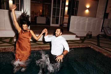 Couple jumping into the pool together at night