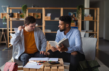 Young happy man with Down syndrome and his tutor studying indoors at school.