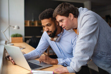 Happy young man with Down syndrome and his tutor using lapotp indoors at school.