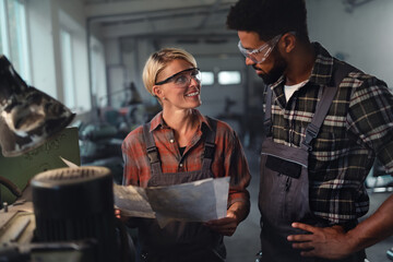 Fototapeta na wymiar Portrait of young biracial industrial colleagues working indoors in metal workshop, smiling.