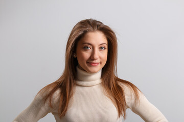 Portrait of a beautiful girl on an isolated gray background. Close-up of a young brown-haired woman in a sweater.