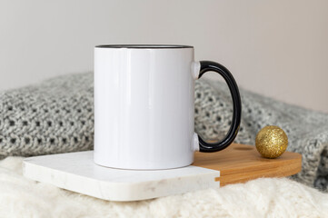 White ceramic coffee cup with black handle mockup on cozy winter background with warm sweaters and...