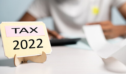 Focus on tax 2022 sign board, unrecognizable man calculating expense or bills behind the tax 2022 sign board - concept of finance, banking and accounting management