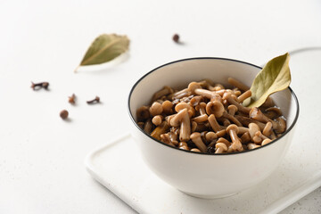 Pickled honey mushrooms in white bowl decorated bay leaves on white background. Tasty homemade appetizer. Copy space. Close up.