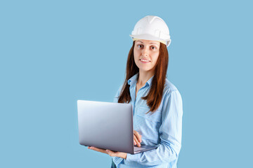Female engineer in hardhat with laptop on blue background, looking into camera