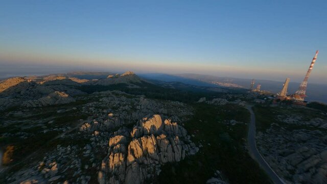 FPV video, mountain surfing, flying at high speed over a granite mountain with an antenna farm during a beautiful sunrise. Mount Limbara (Monte Limbara) Tempio Pausania, Sardinia, Italy.