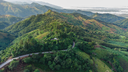 Aerial view of sky road over top of mountain with fog and green jungle after raining in morning, doi sakad, Pua, Nan, Thailand. The transportation by road across beautiful mountain. Shot from drone.