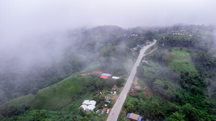 Aerial view of sky road over top of mountain with fog and green jungle after raining in morning, doi sakad, Pua, Nan, Thailand. The transportation by road across beautiful mountain. Shot from drone.