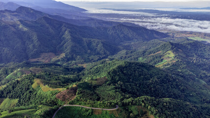 Aerial view of sky road over top of mountain with fog and green jungle after raining in morning, doi sakad, Pua, Nan, Thailand. The transportation by road across beautiful mountain. Shot from drone.