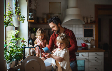 Mature father with two small children washing dishes indoors at home, daily chores concept. - obrazy, fototapety, plakaty