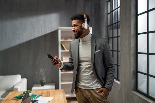 Happy young african american businessman with smartphone and headset working indoors in office