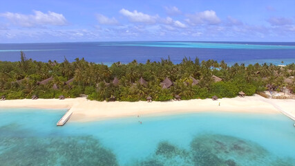 Beautiful resort island in the Maldives, bungalows among palm trees, sandy beach, blue clear water