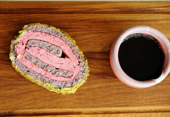 Slice of sponge roll with berries and pistachio and cup of coffee or tea served on wooden board, top view