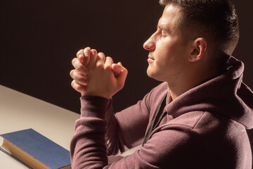 man is praying. Portrait of Prayer guy. Young guy is praying with his eyes closed. Christian folded his palms for prayer. Prayer man on dark background. Book with praying in front of Catholic