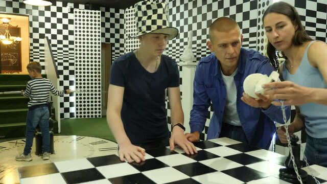 Friendly family of four with two teen boys spending time together in quest room stylized as chessboard, contemplating solving conundrums. High quality 4k footage