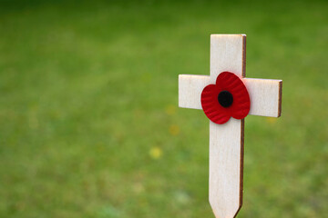 Red puppy flower placed on the small wooden cross in the green grass. Poppy remembrance day cross...