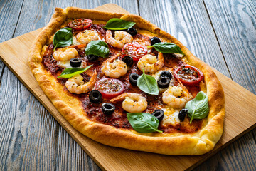 Pizza with prawns, mozzarella, cherry tomatoes and black olives on wooden table
