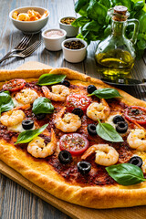 Pizza with prawns, mozzarella, cherry tomatoes and black olives on wooden table
