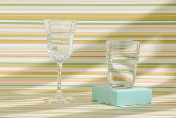 2022 Glasses with healthy fresh clean water against colorful, striped, pastel green orange and beige background. Creative summer arrangement. Reflections of sun and shadows. Natural beverages concept.